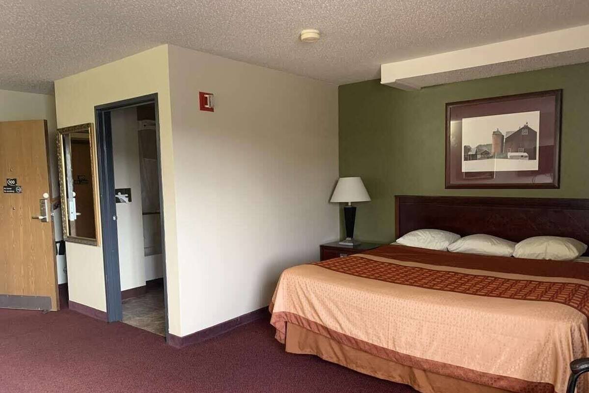 A hotel room with a bed, a nightstand, a lamp, a framed picture on the wall, and an emergency exit sign.