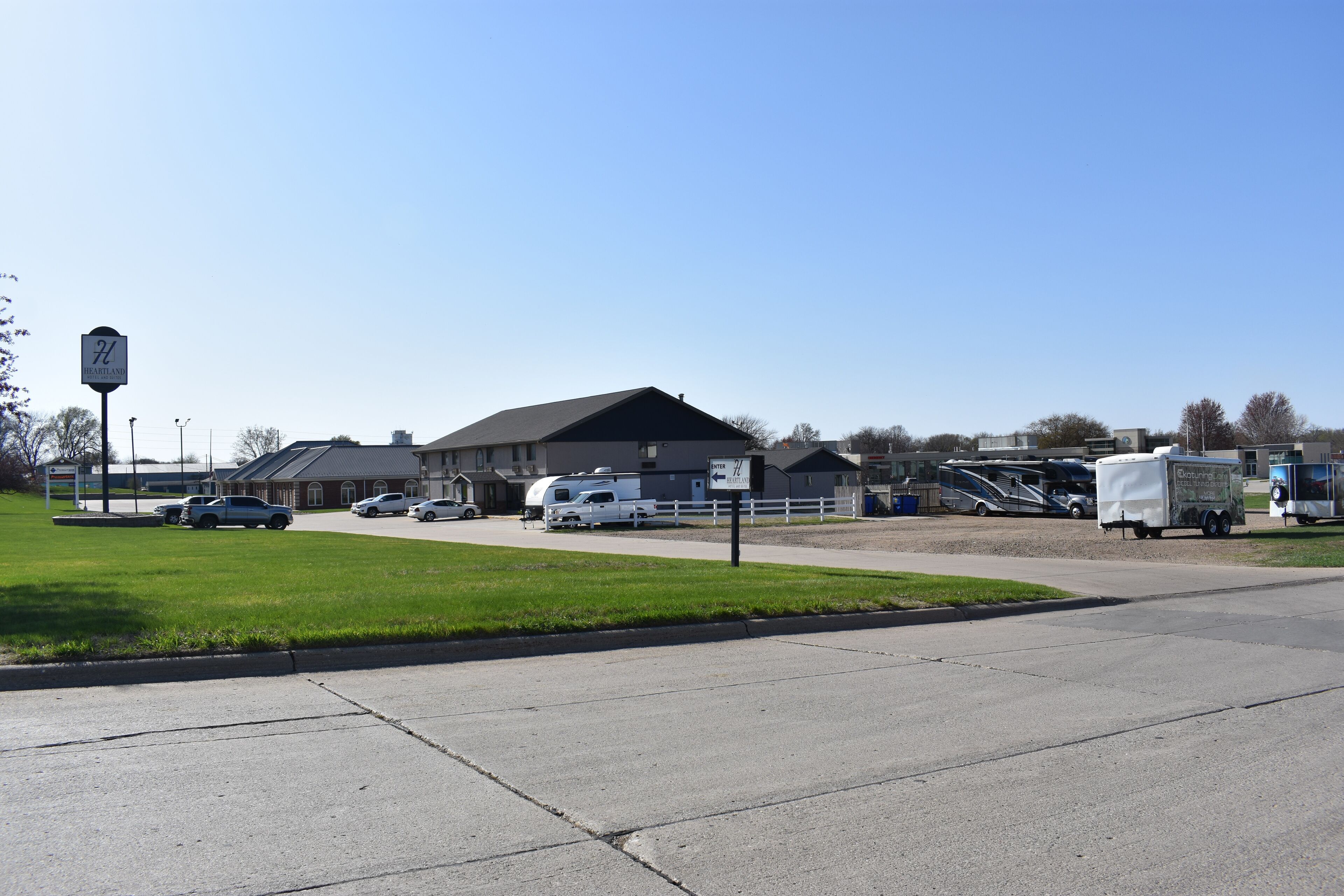 A commercial area with a large building, parked vehicles, and a sign indicating an entrance.