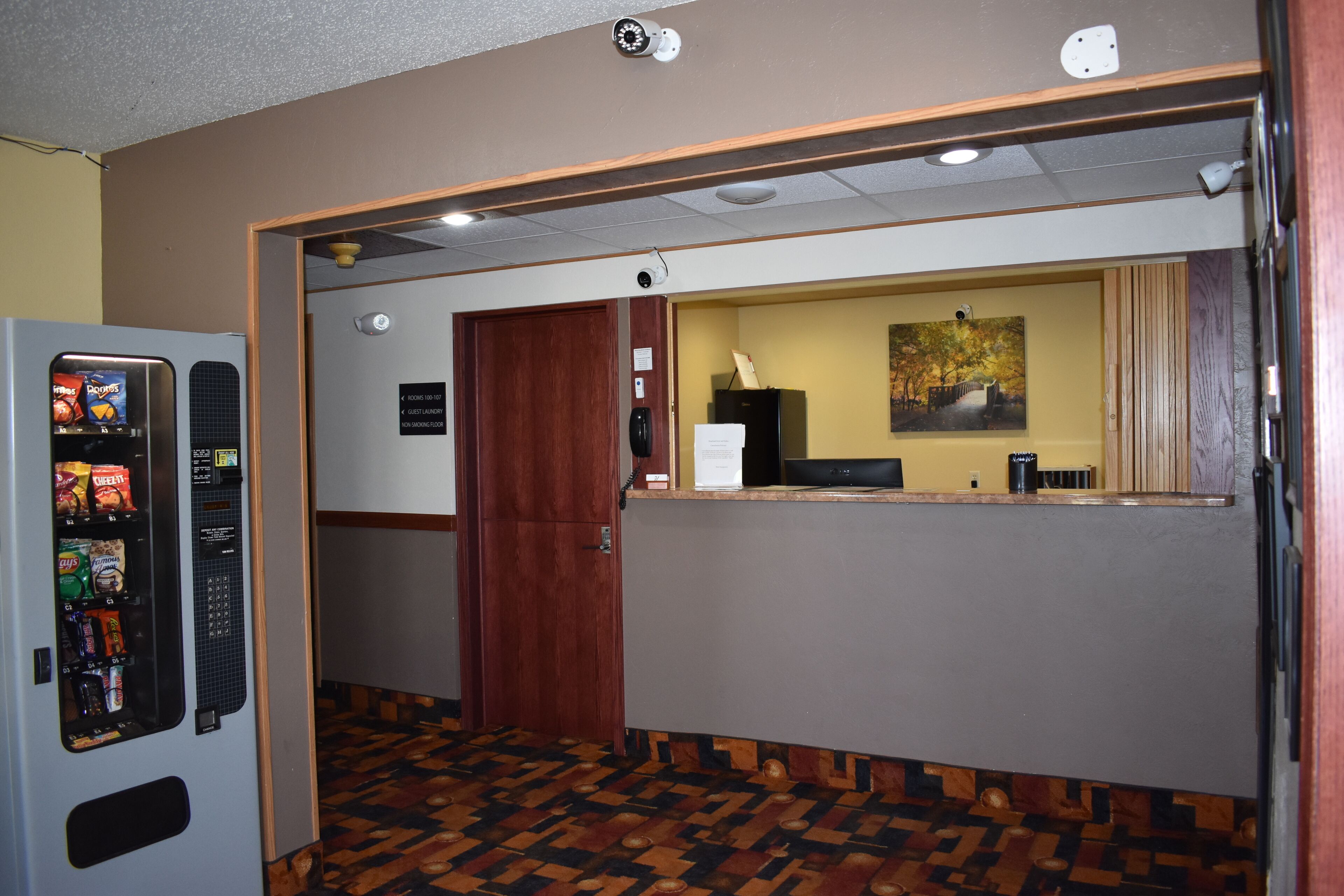 A hotel reception area with a vending machine, a wooden door, and a counter with a painting.