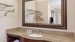 A bathroom with a granite countertop, a white sink, a mirror with a wooden frame, and a towel rack. - Travelodge by Wyndham Sylmar CA (Sylmar)