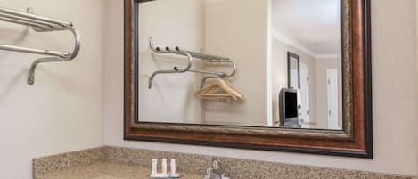 A bathroom with a granite countertop, a white sink, a mirror with a wooden frame, and a towel rack.