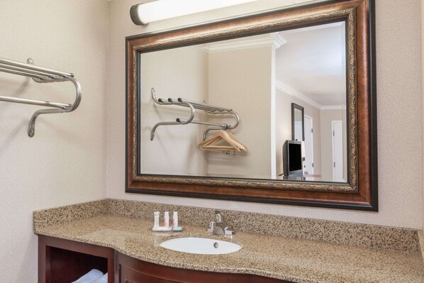 A bathroom with a granite countertop, a white sink, a mirror with a wooden frame, and a towel rack.