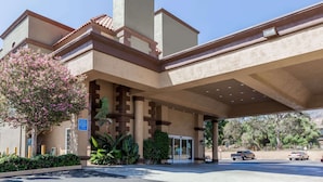 A hotel entrance with a covered parking area, a clear sky, and a vehicle parked outside. - Travelodge by Wyndham Sylmar CA (Sylmar)