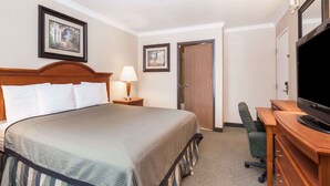 A hotel room with a large bed, a desk with a television, a chair, and two framed pictures on the wall. - Travelodge by Wyndham Sylmar CA (Sylmar)