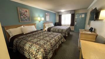 A hotel room with two beds, a desk, a television, and a painting on the wall.