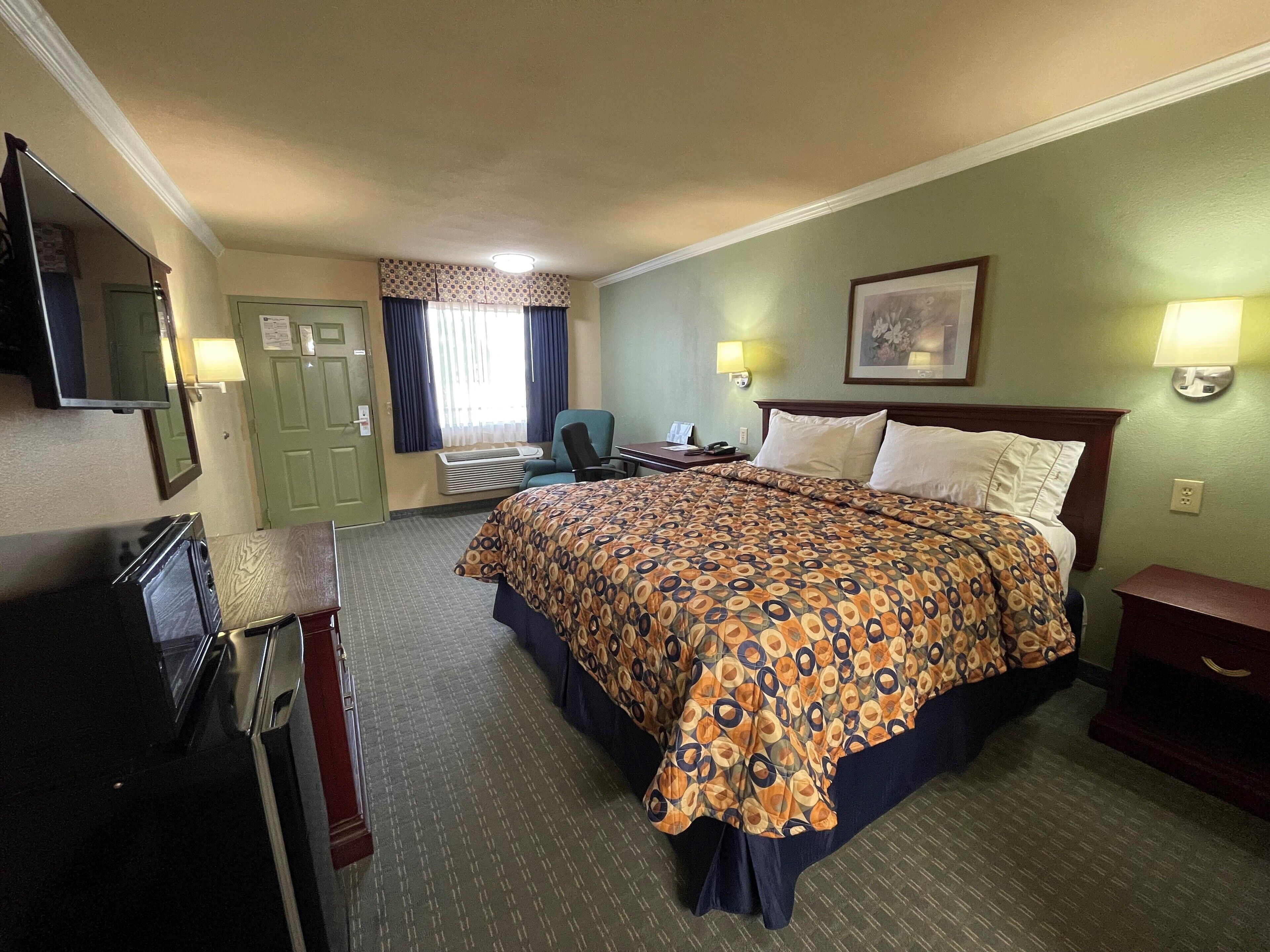 A hotel room with a large bed, a desk, a chair, a TV, and a mirror.