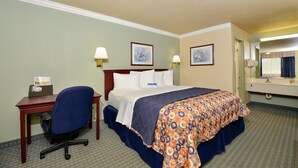 A hotel room with a bed, desk, chair, and a bathroom with a mirror and sink. - Americas Best Value Inn Houston Hobby Airport (Houston)