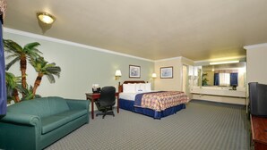 A hotel room with a bed, a desk with a chair, a sofa, a television, and a mirror. - Americas Best Value Inn Houston Hobby Airport (Houston)