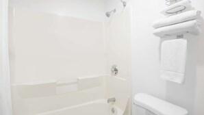 Un baño blanco con bañera, ducha e inodoro. Toallas colgadas en un tendedero.