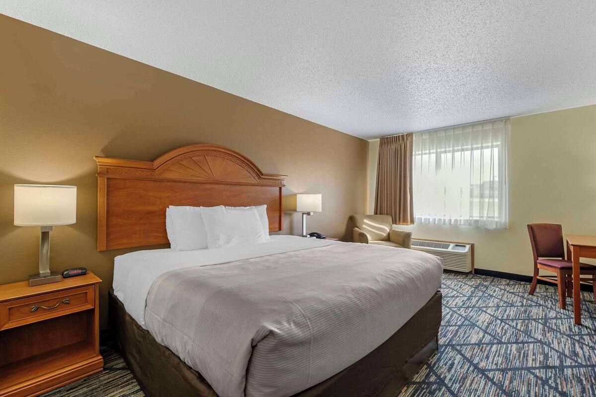 A hotel room with a large bed, two bedside tables with lamps, a chair, a desk, and a window with curtains.