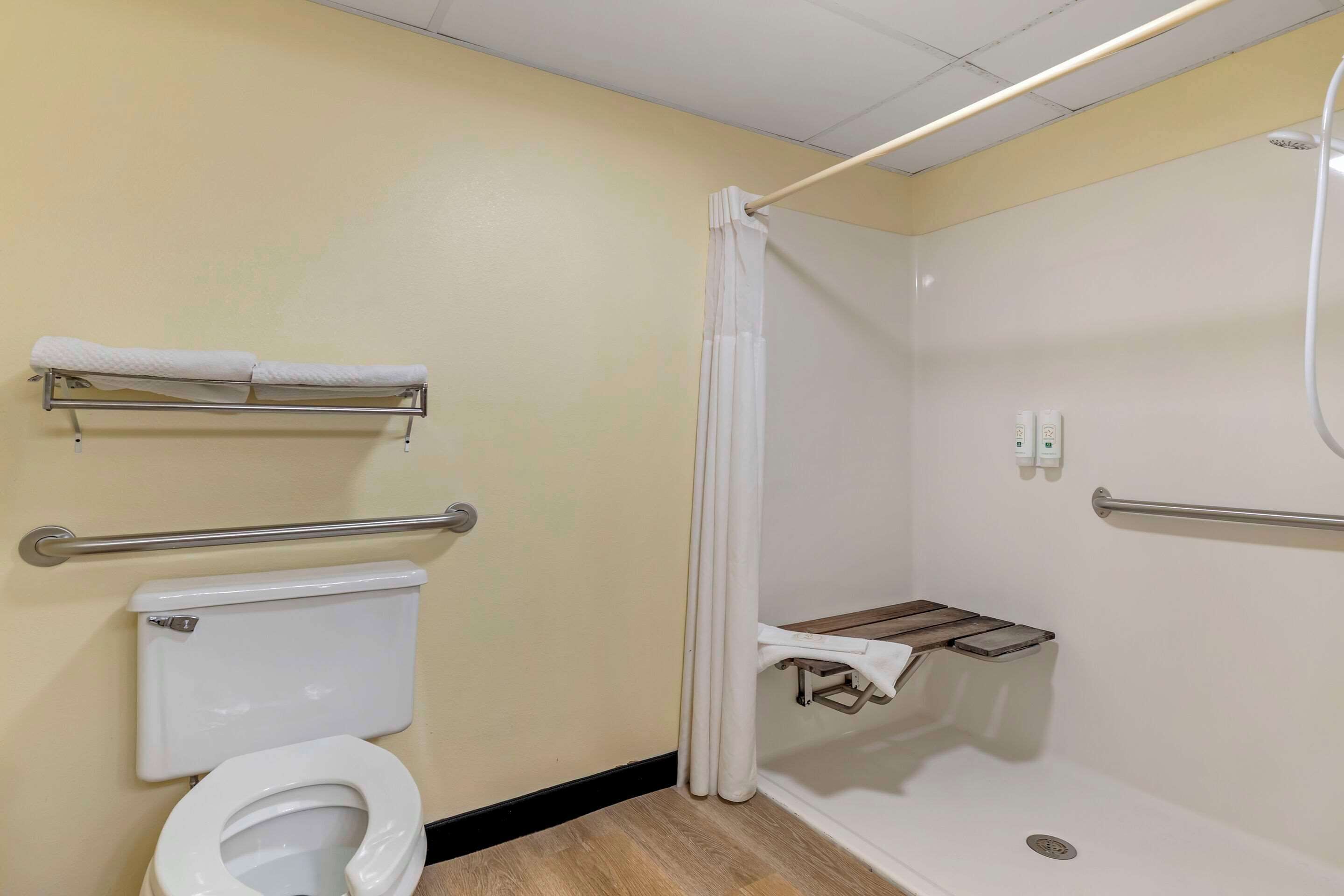 Un baño con inodoro, ducha con barra de apoyo y toallero.