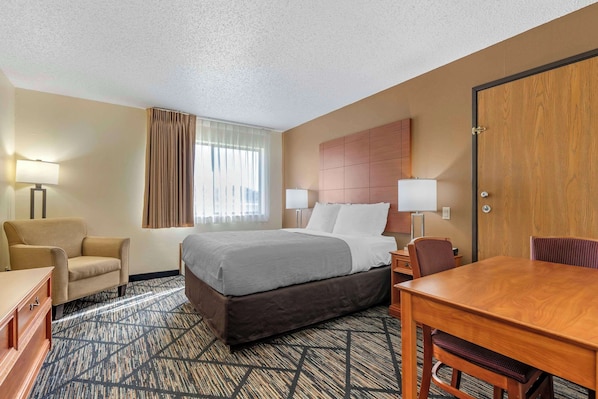 A hotel room with a bed, a desk, a chair, a lamp, and a window with curtains.