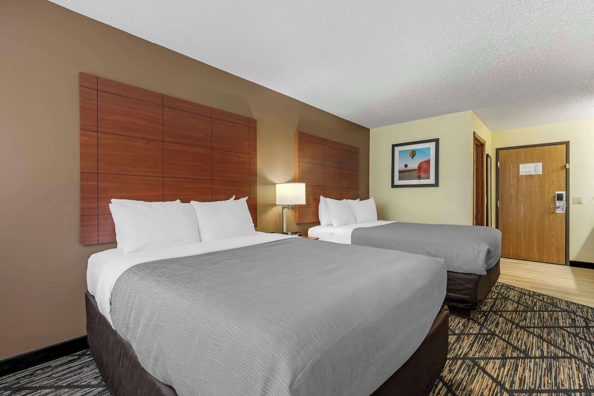 A hotel room with two beds, a wooden headboard, a lamp, and a painting on the wall.