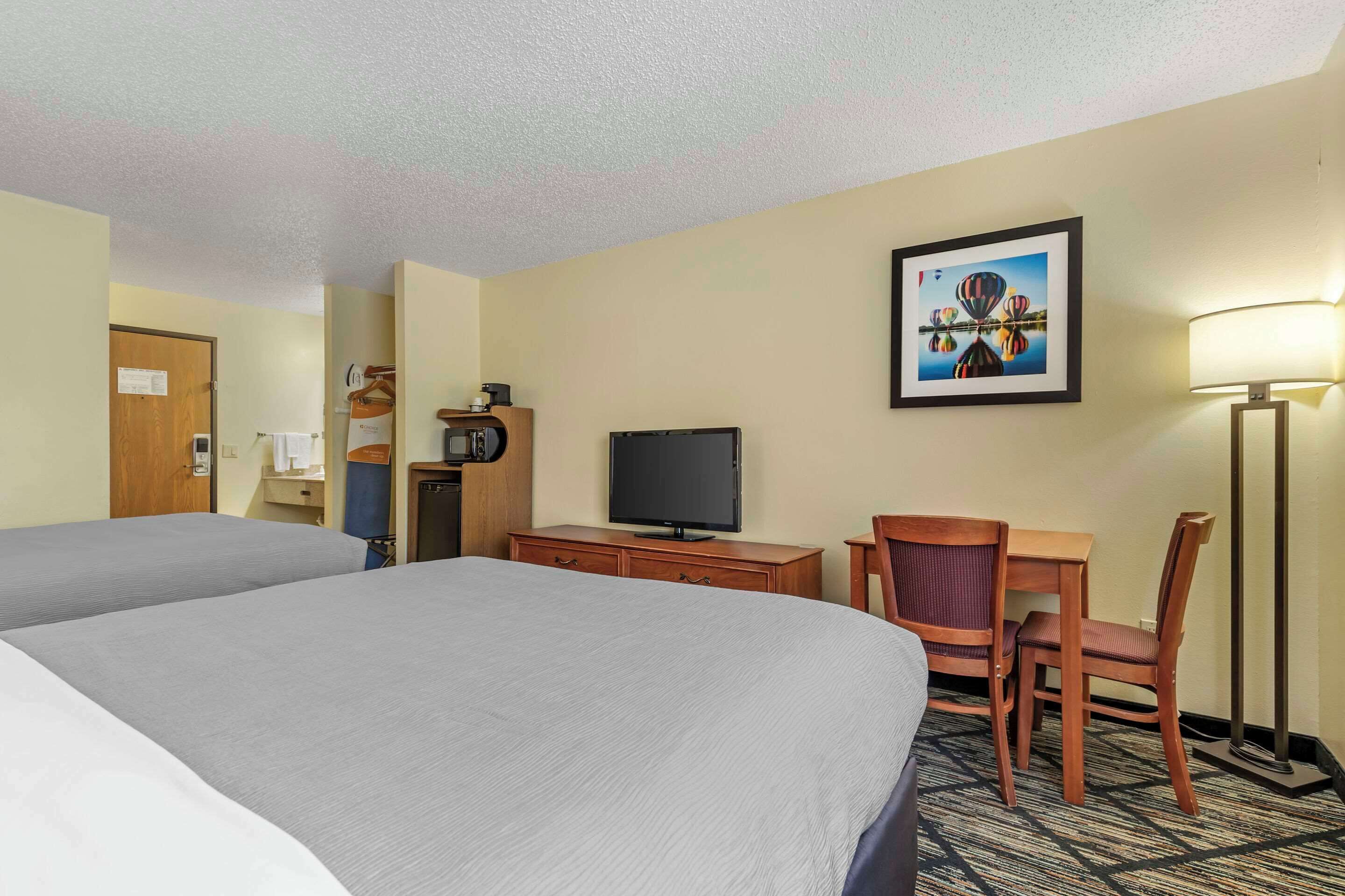 Une chambre d’hôtel avec deux lits, un bureau avec une chaise, une télévision et une lampe.