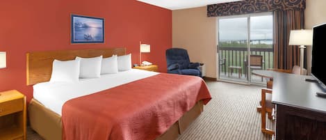 A hotel room with a large bed, a chair, a desk, and a balcony with a view.