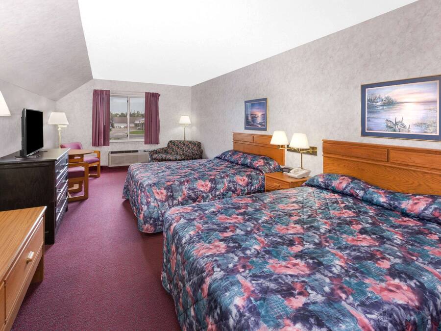 Una habitación de hotel con dos camas, un escritorio, un televisor y un ventanal con cortinas.