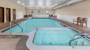 Una piscina interior con agua cristalina, rodeada de sillas de madera y suelo de baldosas.