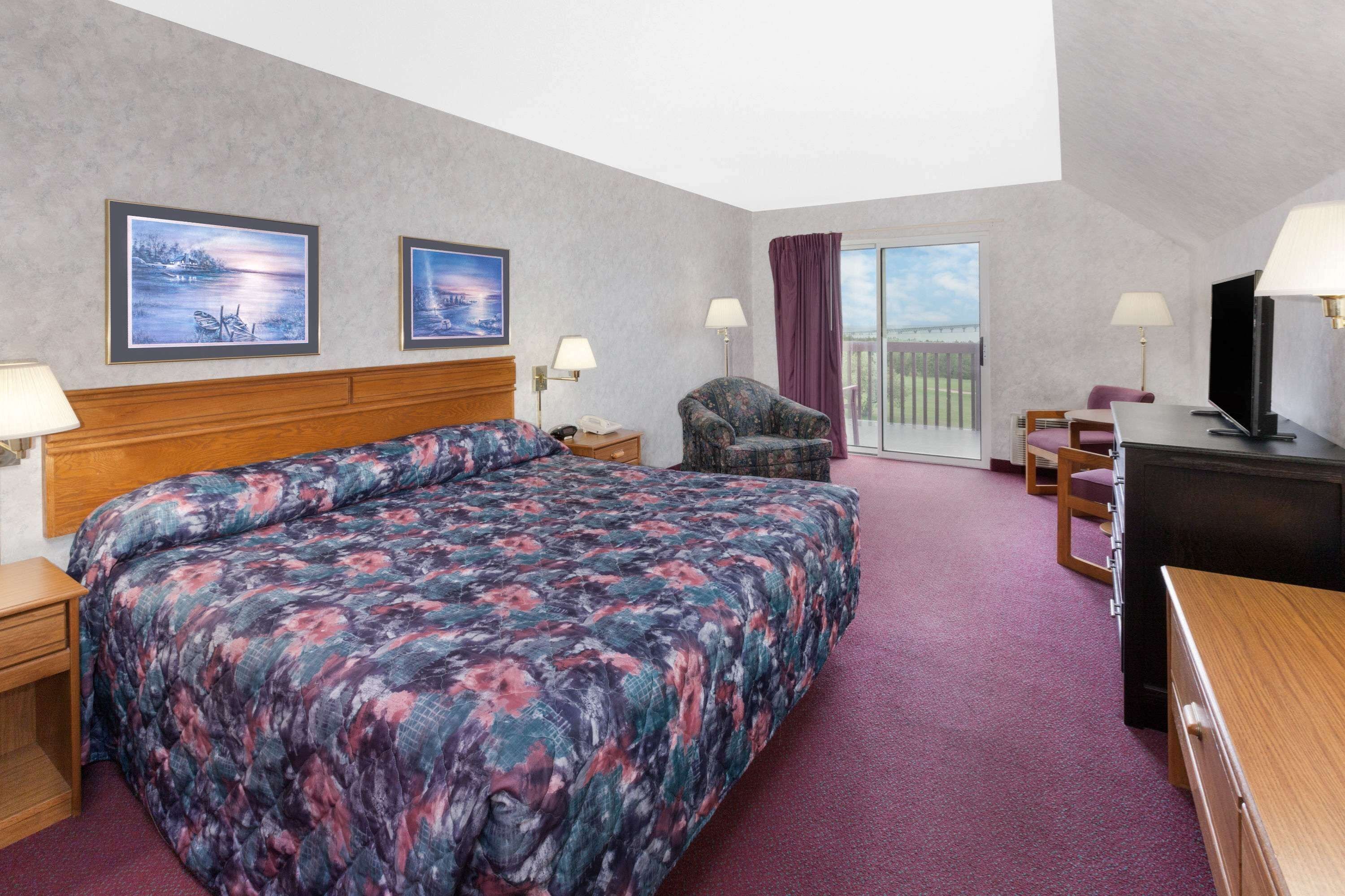 A hotel room with a large bed, a chair, a desk, a TV, and two paintings on the wall.