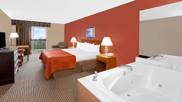 Una habitación de hotel con una cama grande, un área de descanso independiente con una silla y una mesa, un escritorio con una computadora, una bañera grande y una puerta corrediza de vidrio al balcón.