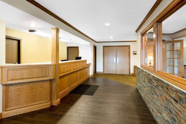 A reception area with a wooden reception desk, a stone accent wall, and a carpeted floor. - Super 8 by Wyndham St. Ignace (St Ignace)