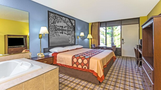 A hotel room with a large bed, a separate bathroom with a bathtub, a desk, and a television.