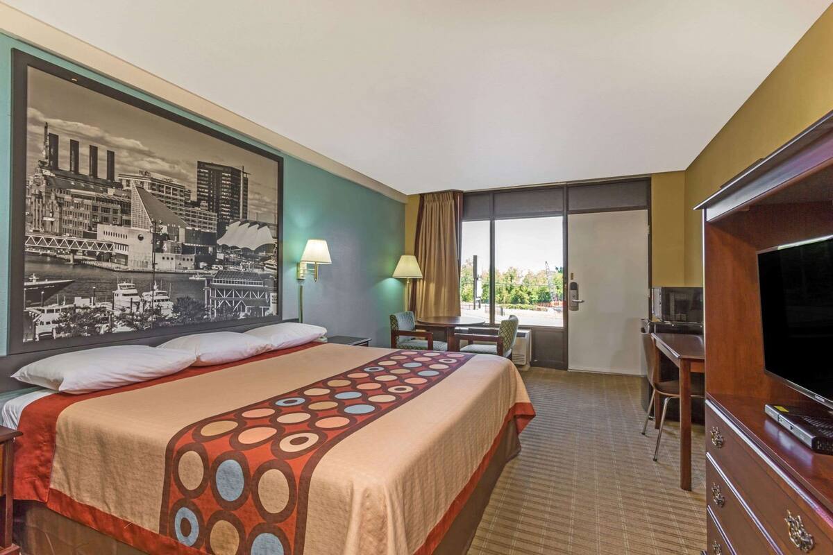A hotel room with a large bed, a desk, a television, and a cityscape mural on the wall.