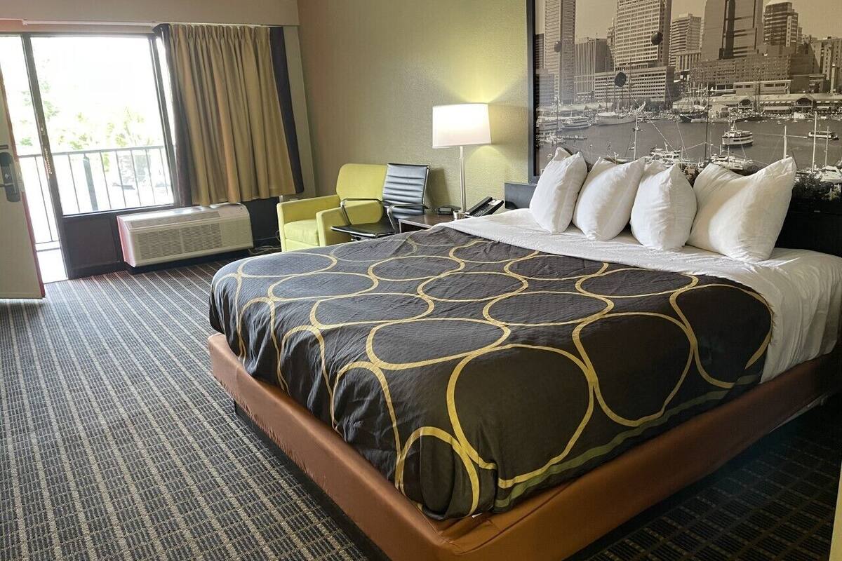 A hotel room with a large bed, a desk, a chair, a lamp, and a cityscape view.