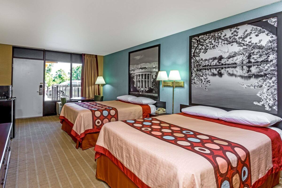 A hotel room with two beds, a large window, and a view of a building and a lake.