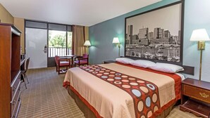 A hotel room with a bed, a desk, a chair, a window with a cityscape view, and two lamps.