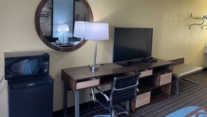 A hotel room with a desk, a television, a microwave, a chair, and a mirror.