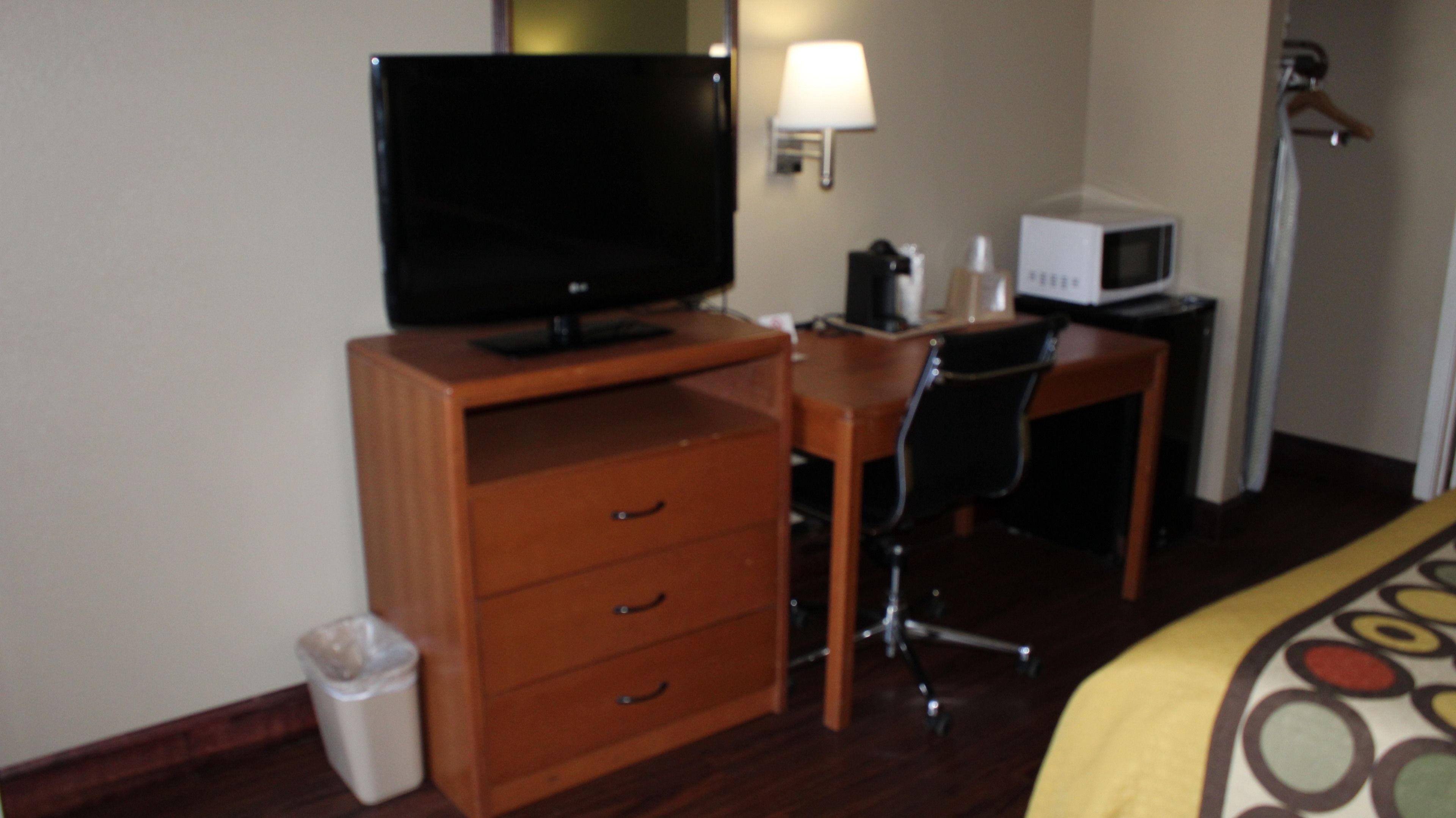 Une chambre d’hôtel équipée d’un bureau en bois, d’une télévision, d’une lampe, d’un four à micro-ondes, d’une chaise et d’une poubelle.