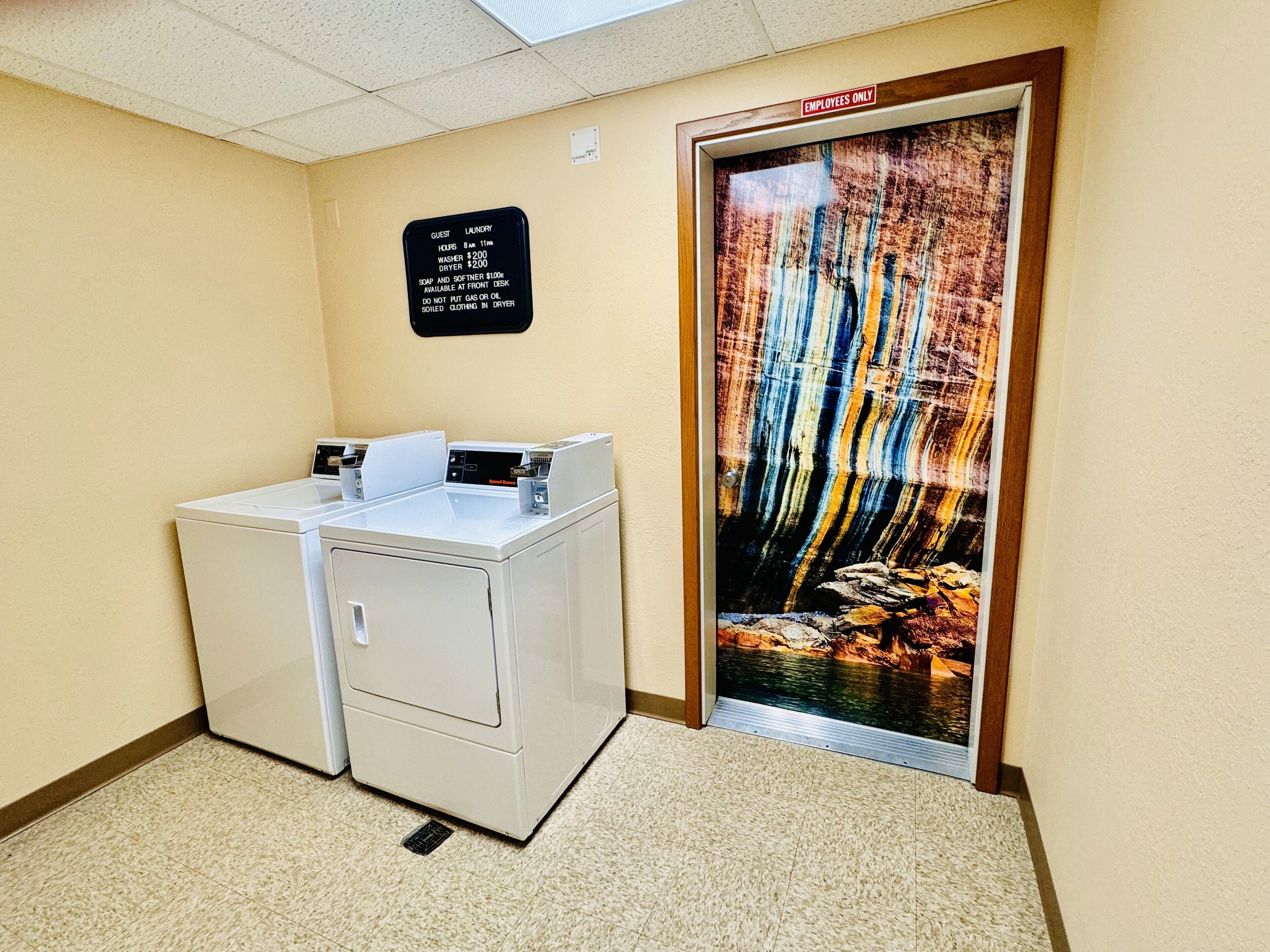 A laundry area with a sign detailing guest laundry hours and fees, a washer and dryer, and a door with an 'Employees Only' sign.
