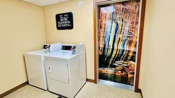 A laundry area with a sign detailing guest laundry hours and fees, a washer and dryer, and a door with an 'Employees Only' sign.