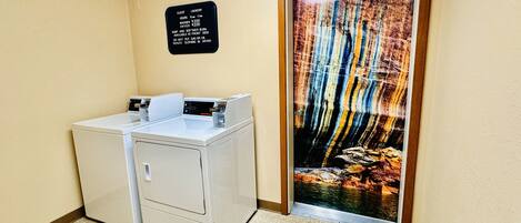 A laundry area with a sign detailing guest laundry hours and fees, a washer and dryer, and a door with an 'Employees Only' sign.