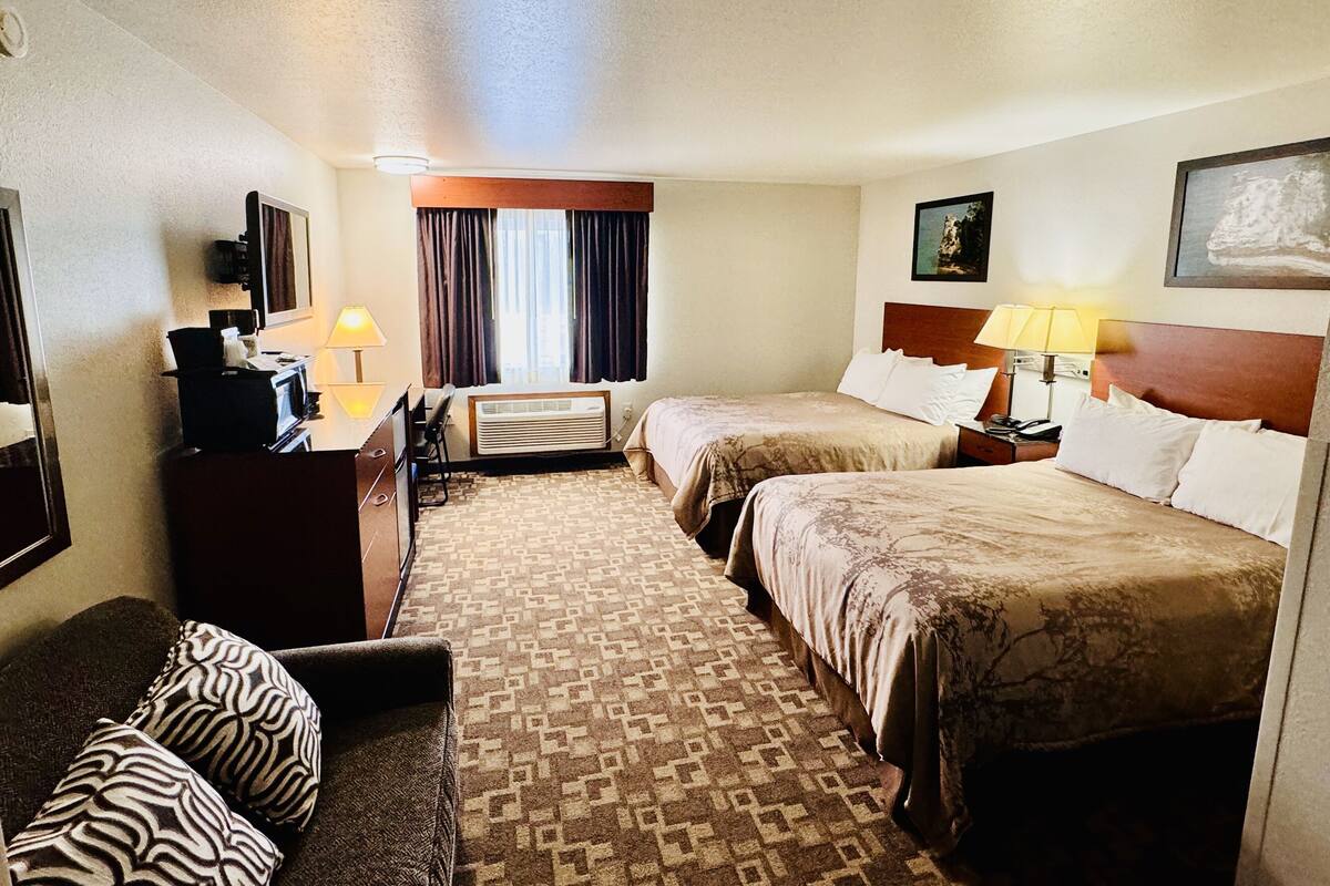 Une chambre d’hôtel avec deux lits, un bureau, une chaise, une télévision et une fenêtre avec des rideaux.