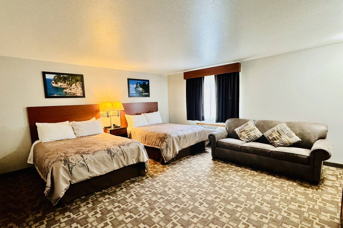Une chambre d’hôtel avec deux lits, un canapé, une moquette à motifs et deux lampes fixées au mur.