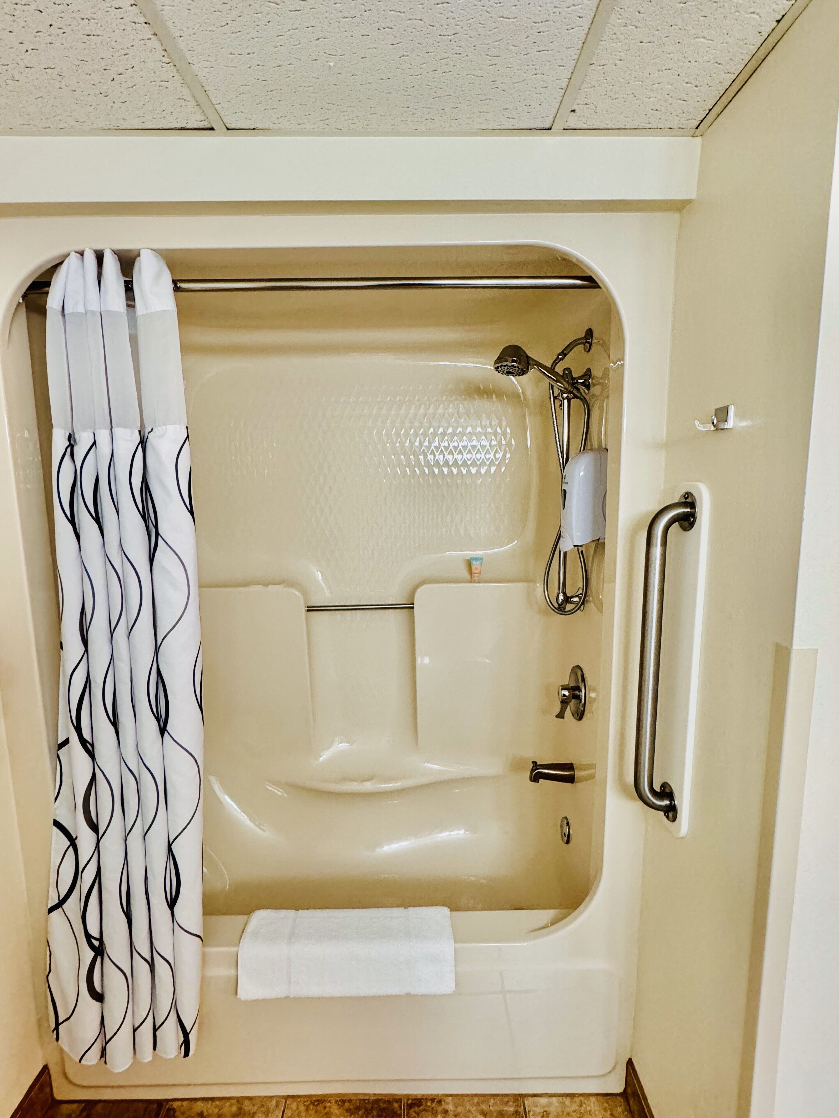 Une baignoire équipée d’une pomme de douche, d’une barre d’appui et d’une serviette.