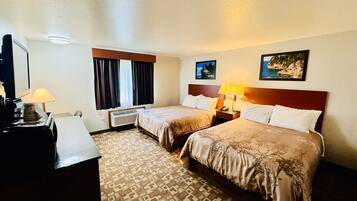 Une chambre d’hôtel avec deux lits, un bureau, une lampe, une fenêtre avec des rideaux, un climatiseur fixé au mur et deux tableaux encadrés.