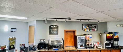 A breakfast counter with a sign indicating breakfast hours, a coffee machine, and a juice dispenser.