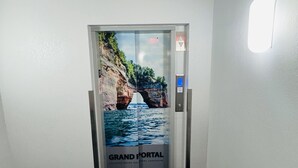 Ein Flur mit Teppichboden, einer Tür mit einem Poster mit einer Küstenansicht und einer Wandleuchte.