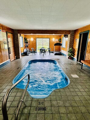 Une piscine intérieure dotée d’un plongeoir de 90 cm de haut, de murs en bois et d’un espace détente avec des chaises et une table.