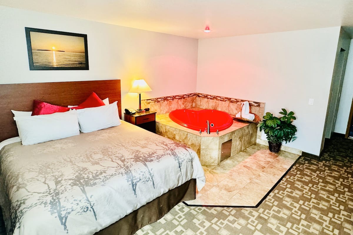 Une chambre d’hôtel avec un lit, une baignoire rouge, une table de chevet, une lampe et un tableau accroché au mur.