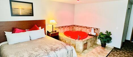 Une chambre d’hôtel avec un lit, une baignoire rouge, une table de chevet, une lampe et un tableau accroché au mur.