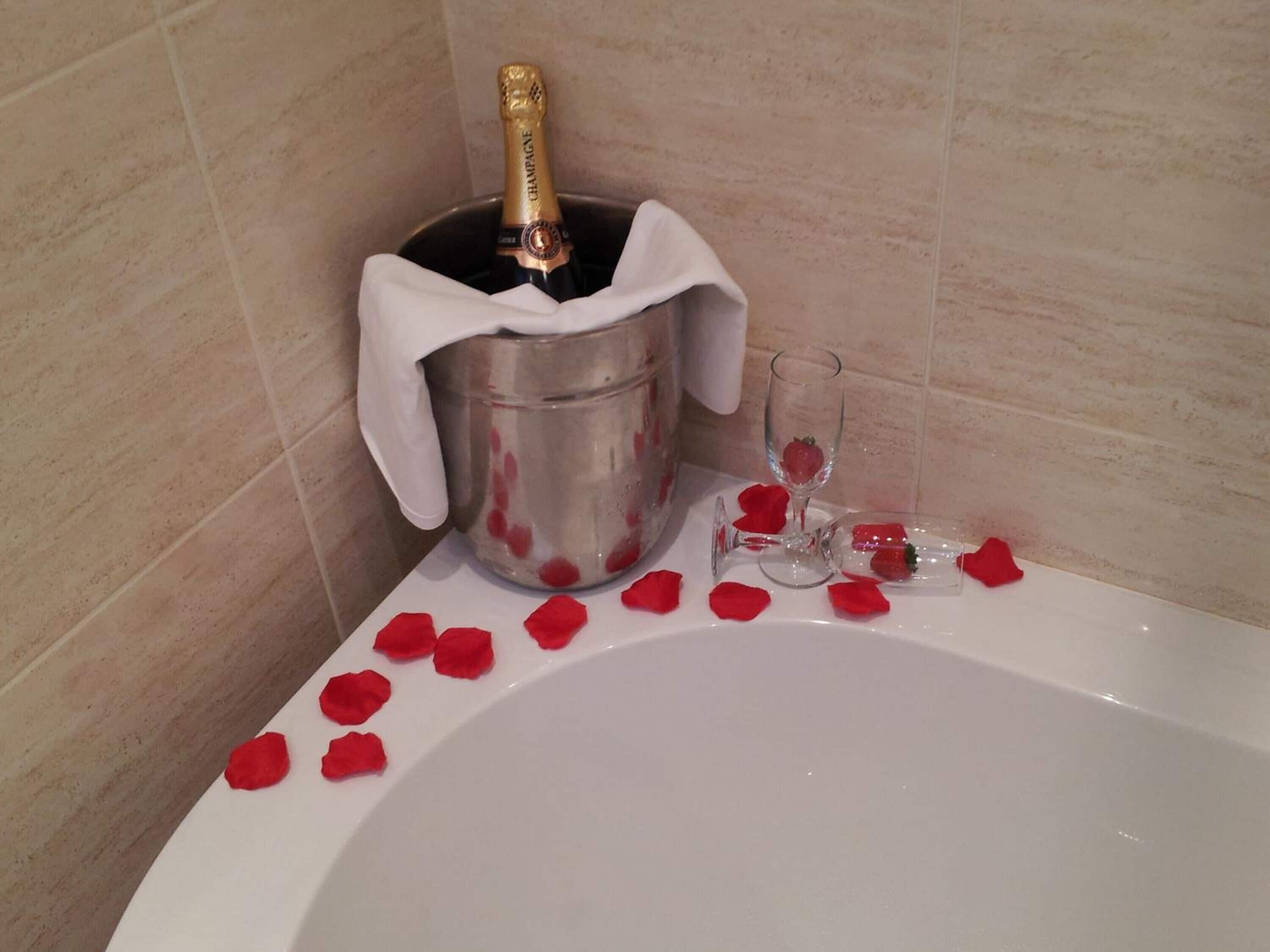 A bathtub with rose petals and a champagne bottle in a bucket.