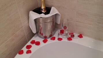 A bathtub with rose petals and a champagne bottle in a bucket.