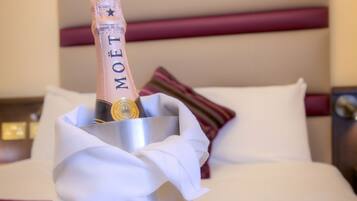 A minibar with a bottle of Moët champagne, two empty wine glasses, and a white cloth napkin on a bed with white bedding and a striped pillow.