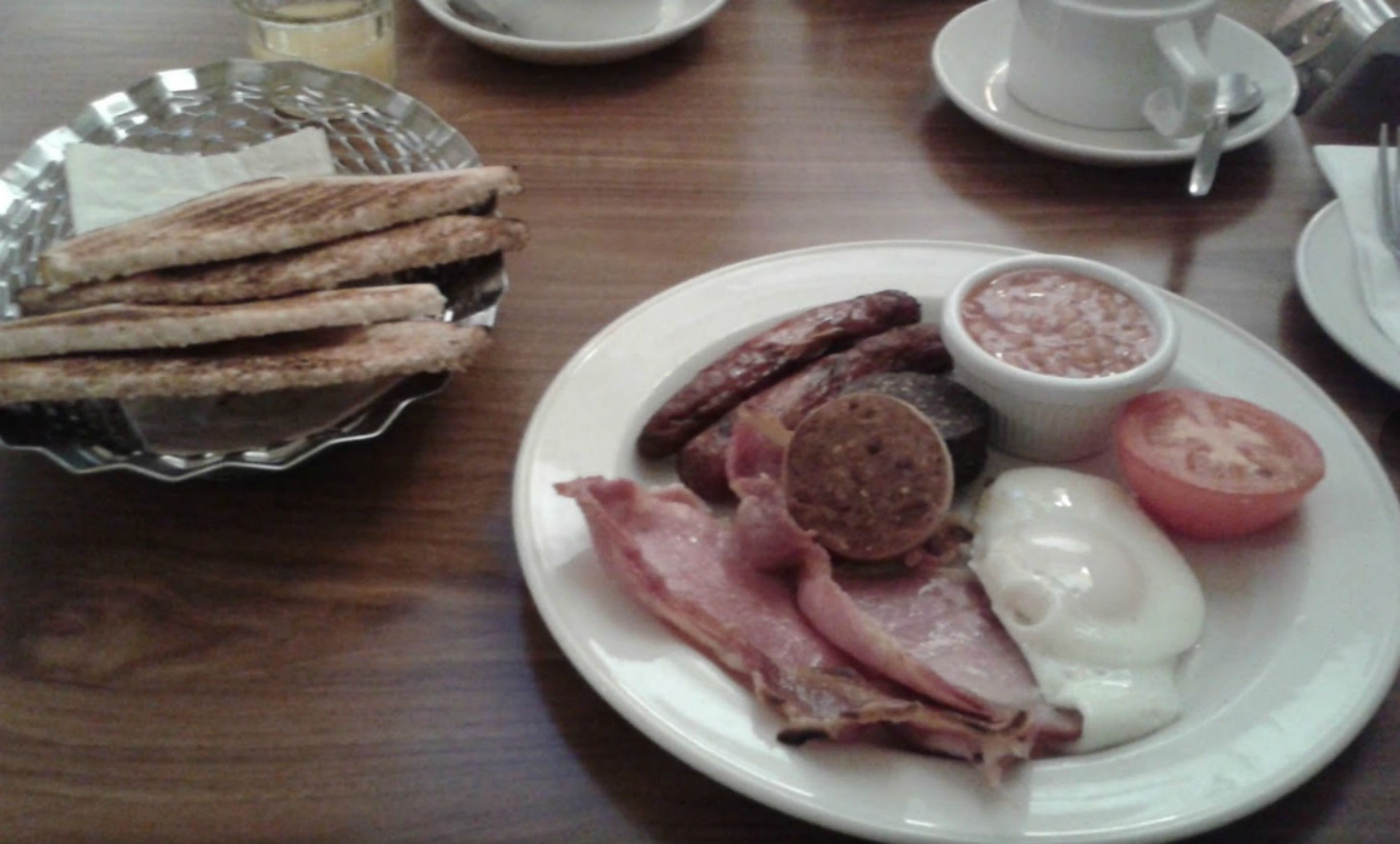 A breakfast plate with eggs, ham, sausages, and a tomato.