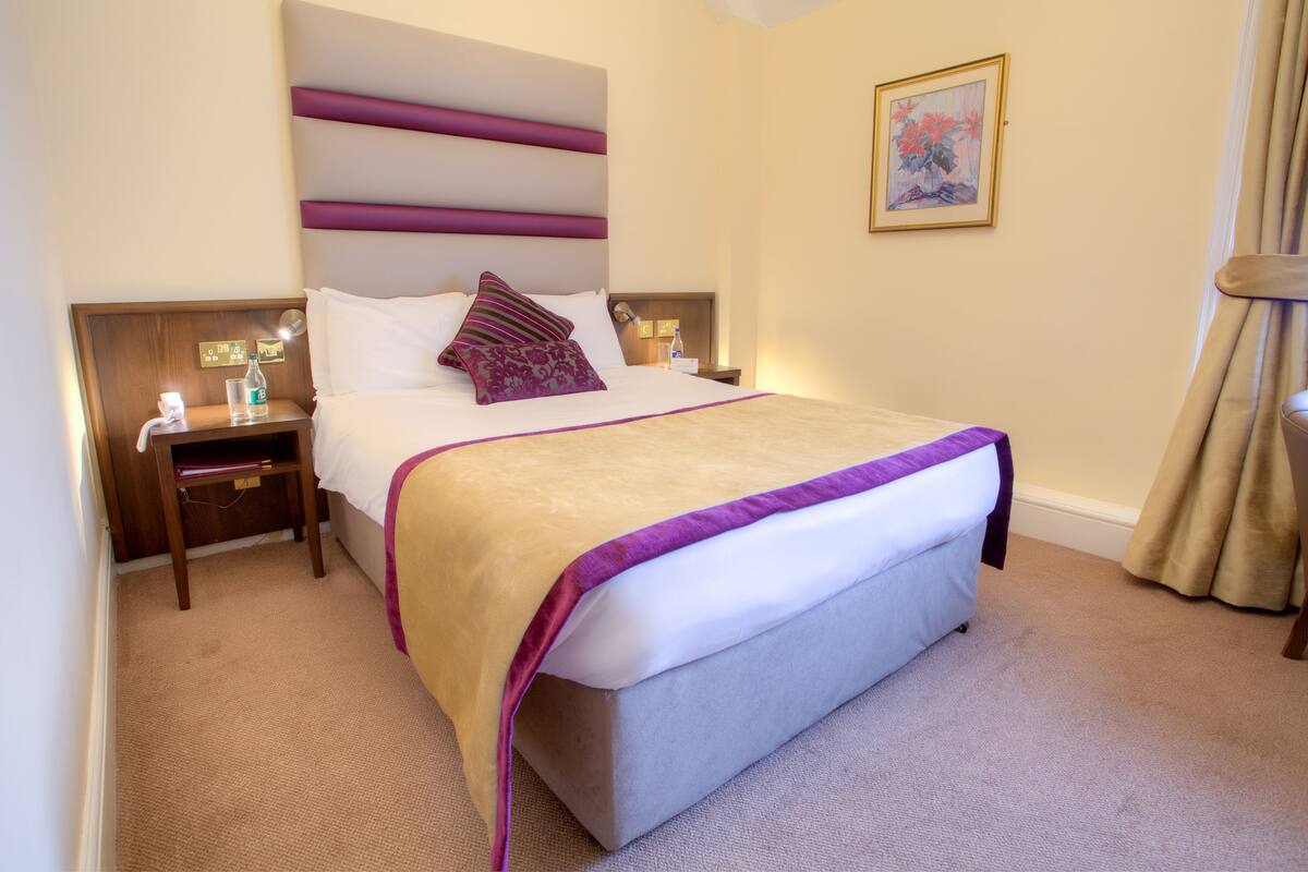 A hotel room with a large bed, a nightstand with a lamp, and a painting on the wall.