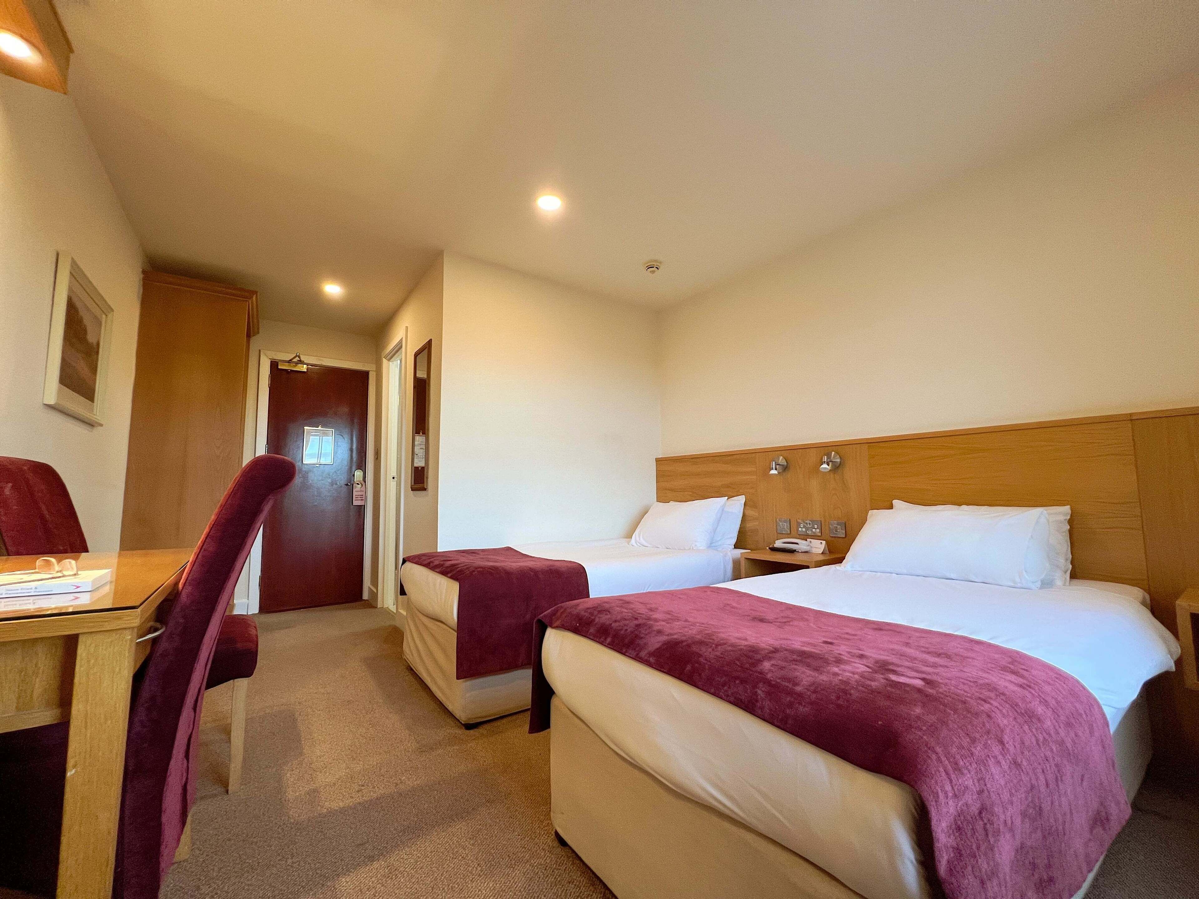 Quarto de hotel com duas camas, uma escrivaninha e uma cadeira.