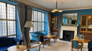 Una habitación con chimenea, paredes azules y un ventanal con cortinas.
